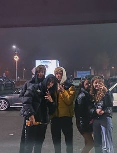 four people posing for a photo in front of a parking lot at night with their hands up