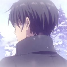 a man with short black hair standing in front of snow covered trees and clouds, looking at the sky