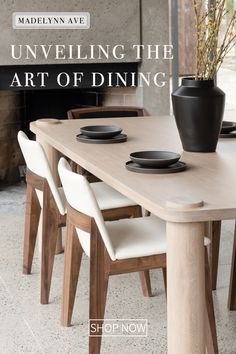 a wooden table with white chairs and a black vase on top of it next to a fire place