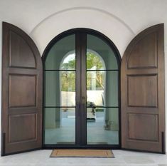 an open door with two arched wooden doors and glass panels on the outside, in front of a white stucco wall