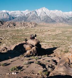 three people sitting on top of rocks in the desert with mountains in the back ground