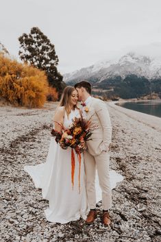 a bride and groom standing together on the beach with mountains in the background at their wedding