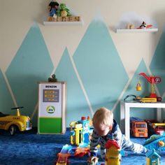 a toddler playing with toys on the floor in front of a wall painted with mountains