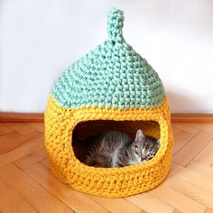 a cat in a crocheted ball bed on the floor next to a wall