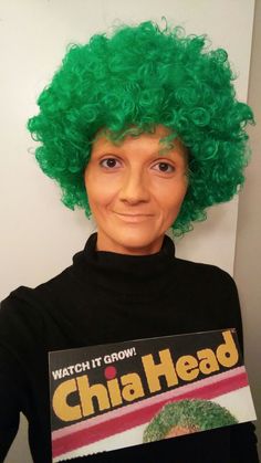 a person wearing a green wig and holding a sign that reads watch it grow chia head