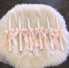 four white candles with pink bows are arranged on a fur rug in front of a black background