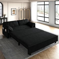 a black couch sitting on top of a rug in a living room next to windows