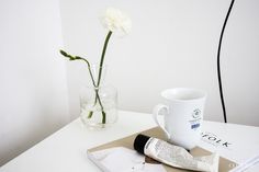 a white flower sitting on top of a table next to a coffee cup and magazine