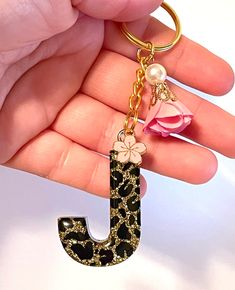 a hand holding a key chain with a letter shaped like a leopard print and flowers