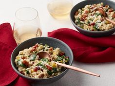 two bowls filled with pasta and vegetables on top of a red napkin next to a glass of wine