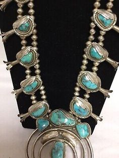 an old necklace with turquoise stones and silver beads on a black mannequin stand