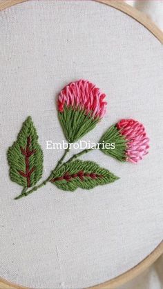 two pink flowers with green leaves are on a white surface in front of a wooden hoop