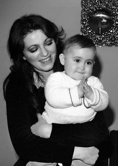 a black and white photo of a woman holding a baby in her arms, smiling at the camera