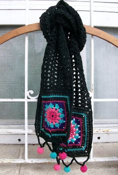 a black crocheted scarf hanging on a window sill with pom - poms