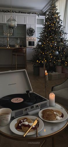 a christmas tree is in the living room next to a table with food on it