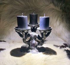 two candles sitting on top of a silver candle holder in the shape of a skull