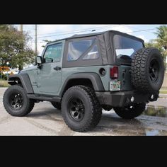 a green jeep parked in a parking lot next to a palm tree and street sign