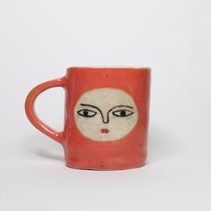 a red and white coffee cup with a face painted on the side, in front of a white background