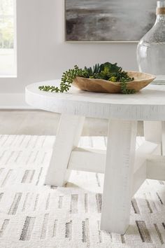 a white table topped with a bowl of green plants