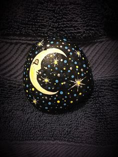 a painted rock with the moon and stars on it, sitting on a black blanket