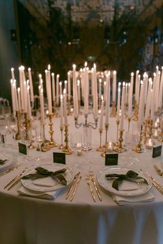 a white table topped with lots of plates and silverware next to tall lit candles