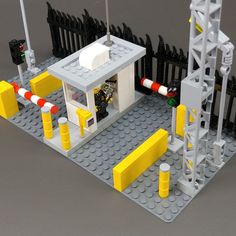 a lego model of a small building with yellow and white barriers around it, on top of a gray surface