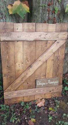 a wooden crate sitting on the ground next to some leaves and plants in front of a fence