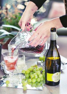 a woman pours wine into a glass on a table with grapes and other items