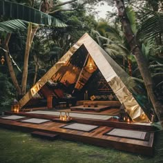 an outdoor tent set up in the middle of some trees with candles lit on it