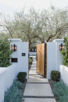 an entrance to a home with white walls and wooden doors, surrounded by greenery