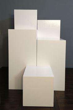 three white cubes stacked on top of each other in front of a gray wall