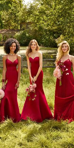 three bridesmaids in red dresses posing for the camera with pink flowers and greenery