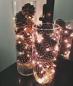 pine cones are sitting in glass vases with lights on the inside and around them