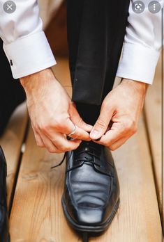 the man is tying his shoes on the wooden floor in order to get ready for the wedding