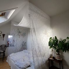 a bed with a white canopy in a bedroom next to a potted plant on a table