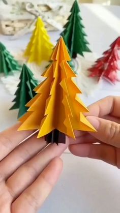 someone is holding an origami christmas tree in front of some other paper trees