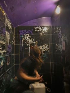 a woman sitting on top of a toilet in a room with graffiti all over the walls