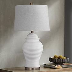 a white lamp sitting on top of a wooden table next to a book and vase