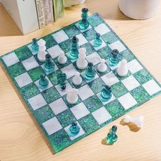 a glass chess board on a table with pieces scattered around it and books in the background