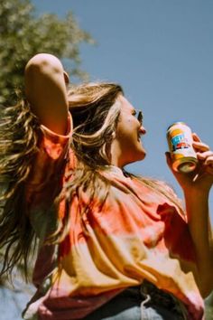 a woman with her hair blowing in the wind and holding a can of beer up to her ear