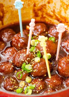 meatballs with toothpicks in a red sauce and garnished with green onions