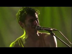 a man singing into a microphone in front of a green background with light coming from behind him