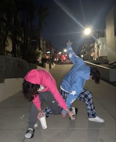 two people doing tricks on the sidewalk at night