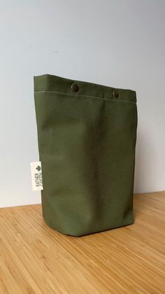 a green canvas bag sitting on top of a wooden table next to a white wall