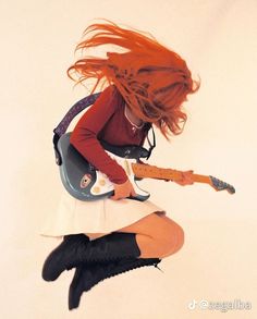 a girl with red hair is playing an electric guitar and jumping up in the air