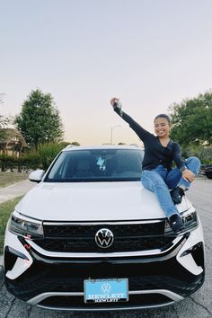 a woman is sitting on the hood of a white car with her arms in the air