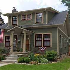 a gray house with red trim and american flags on the front