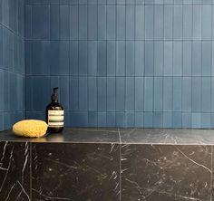 a bottle of soap and sponge sit on a counter in a blue tiled bathroom area