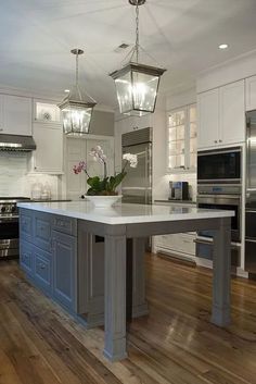 a large kitchen with an island in the middle and two lights hanging from the ceiling