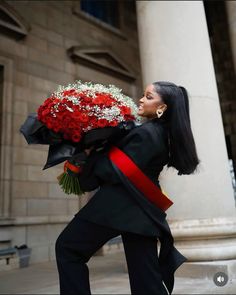 a woman holding flowers in her hands while walking down the street